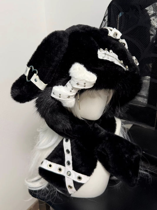 Hardcore black plush bunny ear hood on a mannequin, decorated with silver safety pins, metal eyelets, and a dangling silver cross charm.