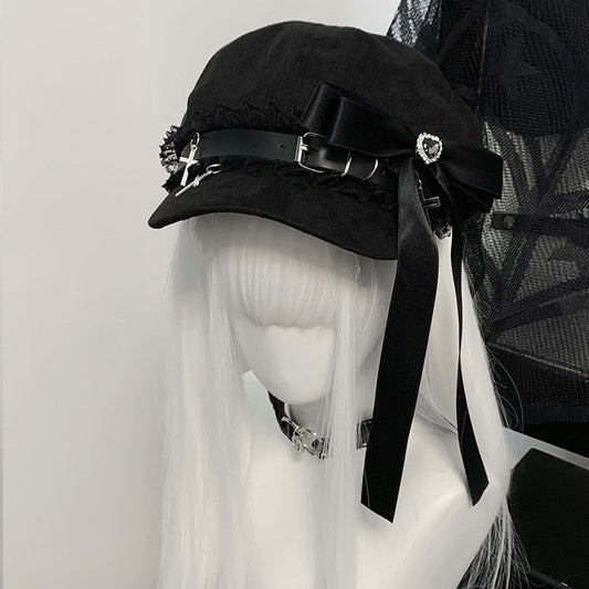 Black Jirai Kei newsboy cap on a white-haired mannequin, featuring a large black satin ribbon, lace trim, and silver cross charms.