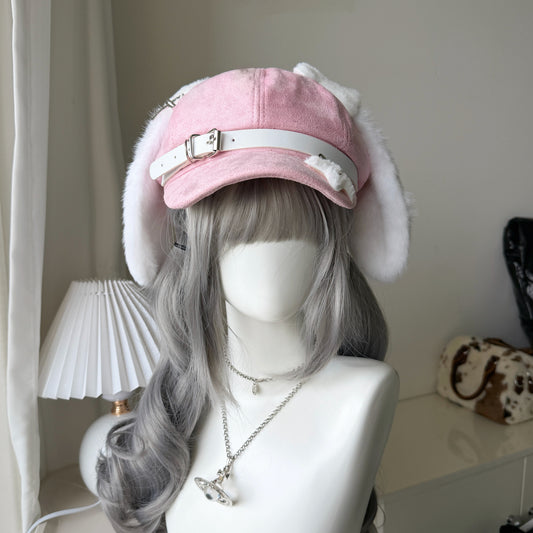 Pink newsboy cap with long white plush dog ears and a white leather belt buckle strap on a mannequin with grey hair.