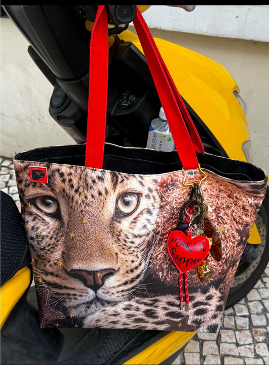 Leopard print tote bag with red handles and heart-shaped charm on a yellow vehicle.