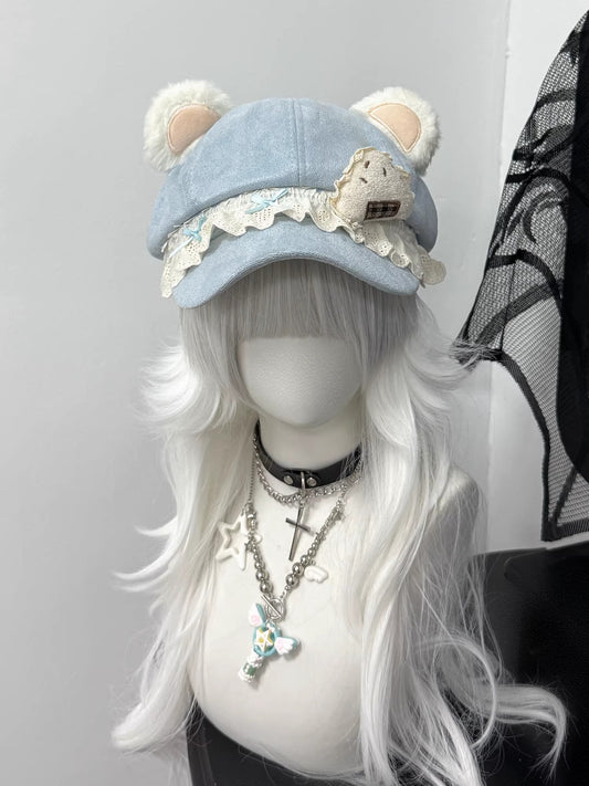 Blue newsboy cap with plush bear ears and white lace brim, decorated with a checkered cupcake patch, styled on a white wig with a gothic cross necklace.