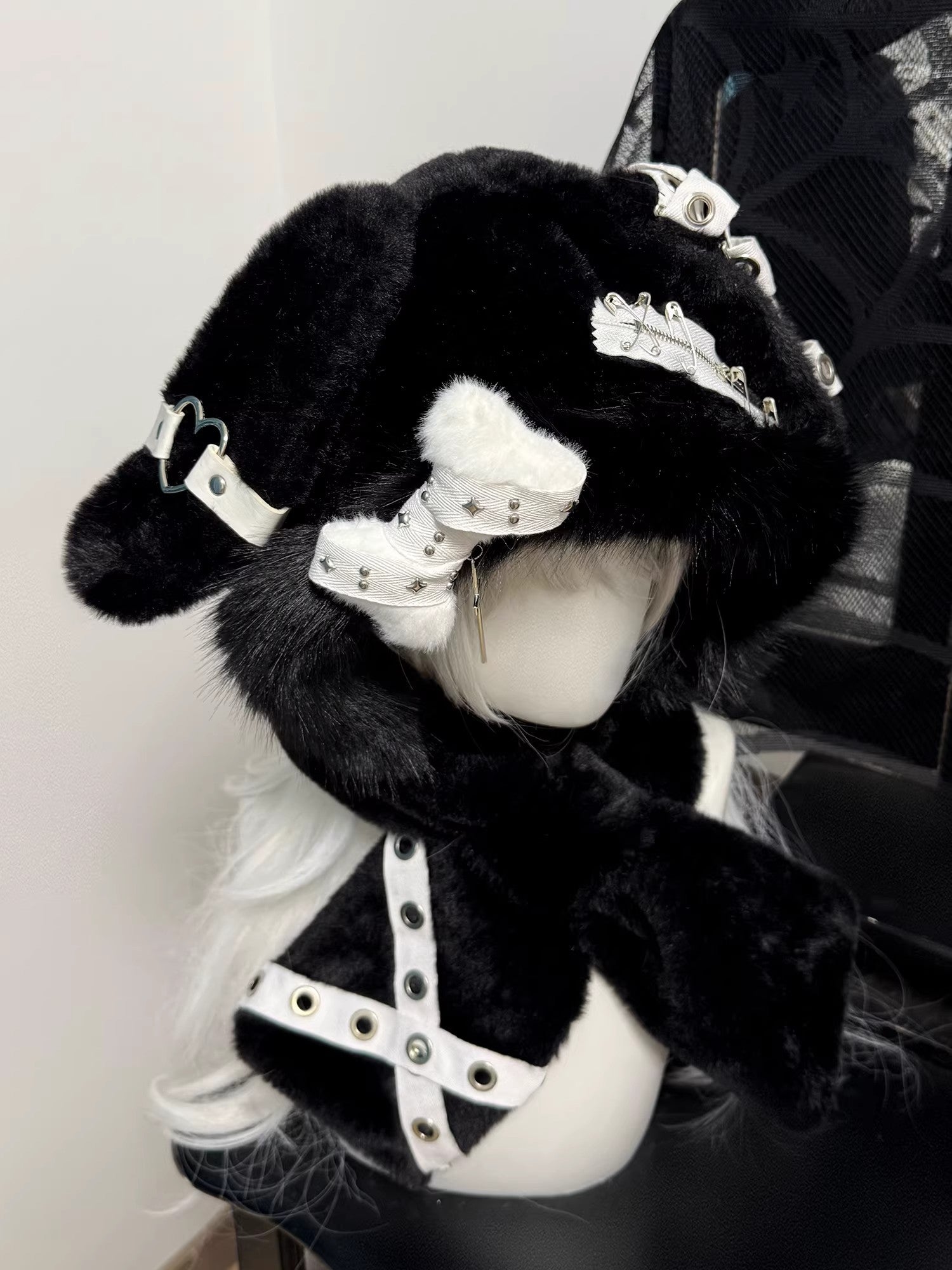 Hardcore black plush bunny ear hood on a mannequin, decorated with silver safety pins, metal eyelets, and a dangling silver cross charm.