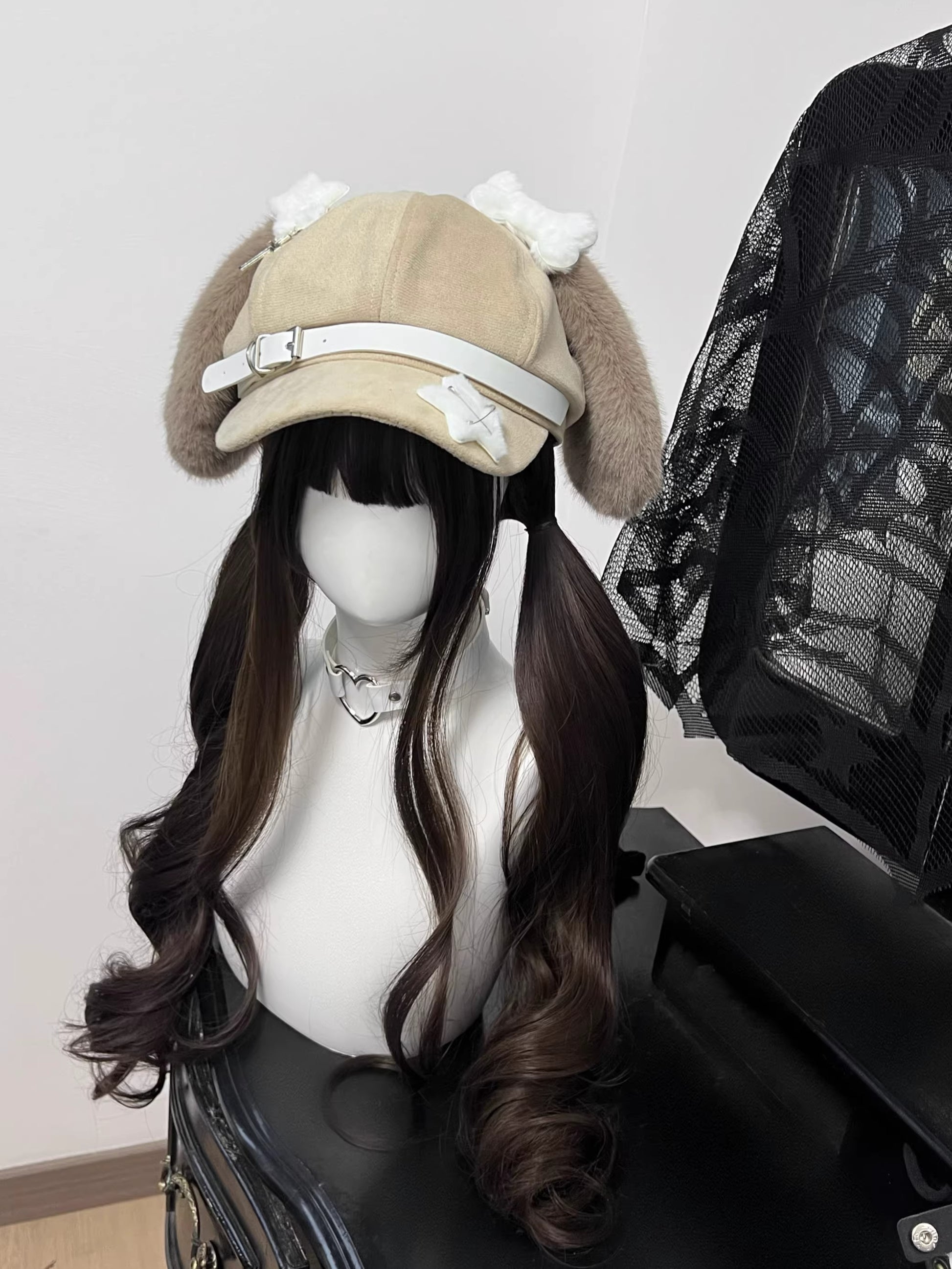 Light khaki suede newsboy cap with long floppy puppy ears, black leather strap accents with metal buckles, and white contrast stitching.