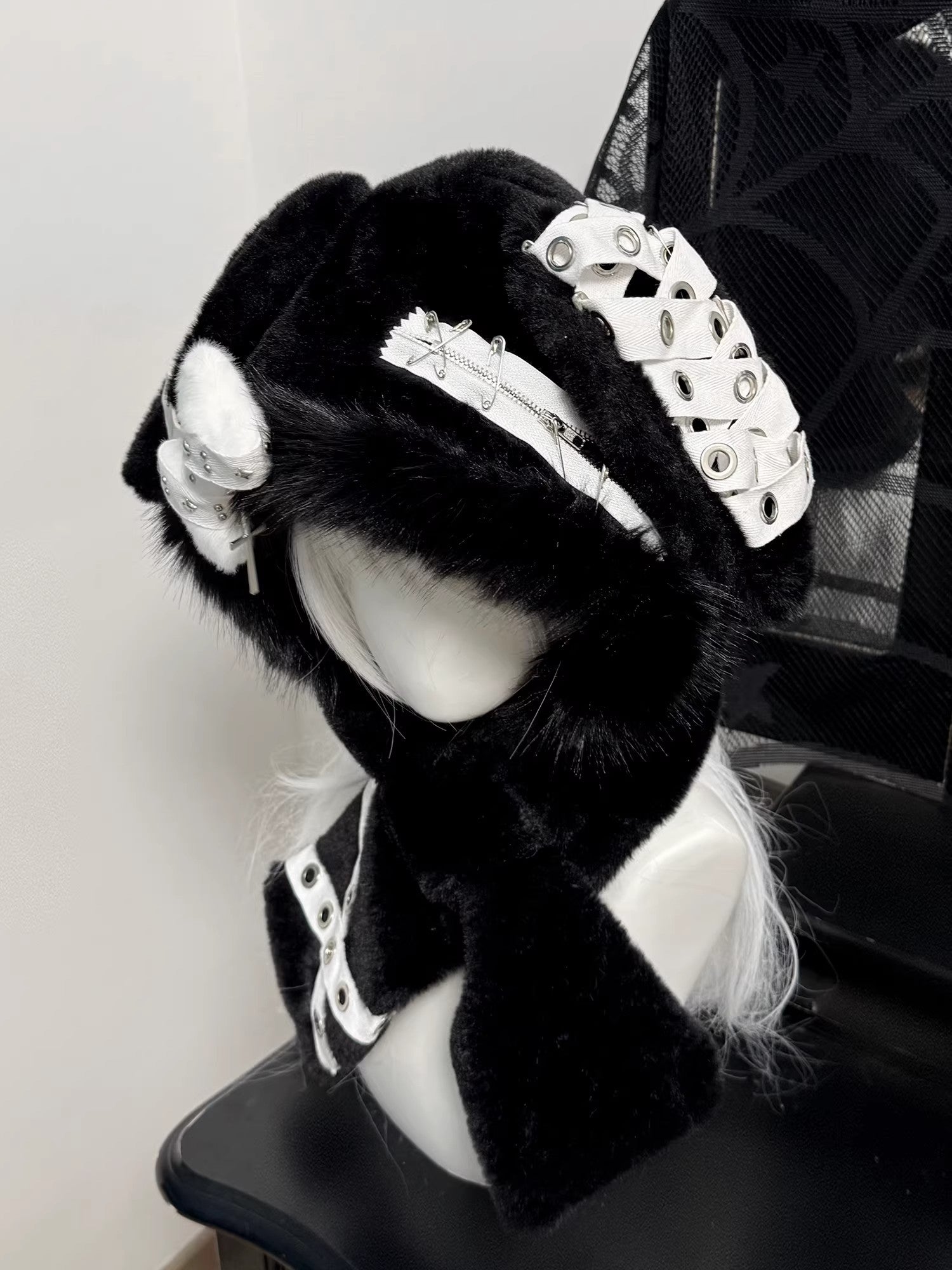 Hardcore black plush bunny ear hood on a mannequin, decorated with silver safety pins, metal eyelets, and a dangling silver cross charm.