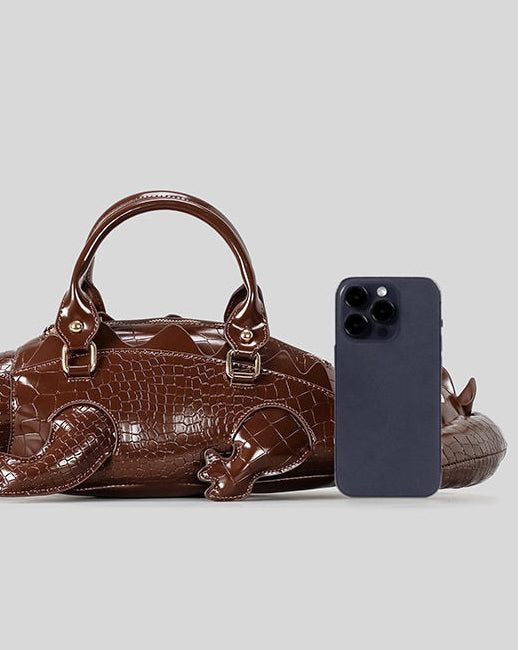 A brown crocodile-shaped handbag shown next to a smartphone for size comparison on a light gray background, with Chinese text at the top reading 'Comparing the size'.