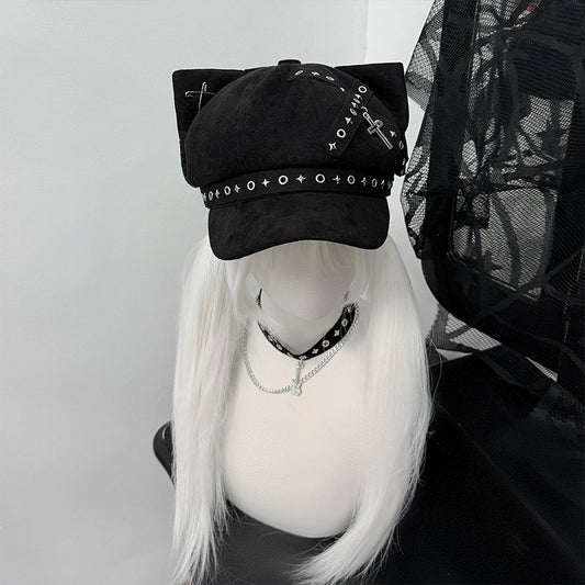 Black cat ear newsboy cap with metal cross charms, safety pins, and grommet webbing on a white-haired mannequin, gothic alt style.