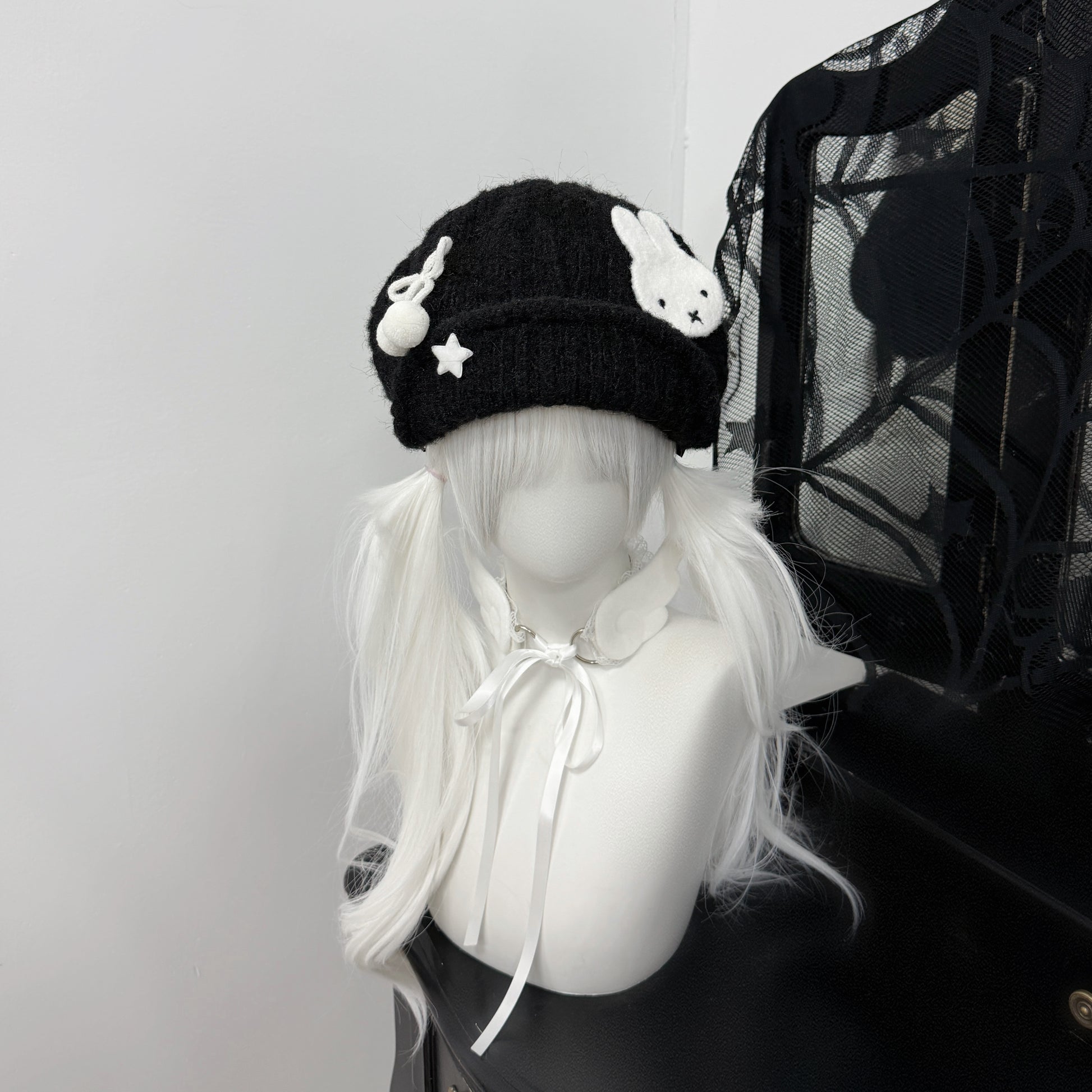 Close-up of a black knit beret hat featuring a white Miffy bunny patch and star charms on a mannequin with white pigtails, Y2K Harajuku style fashion accessory.