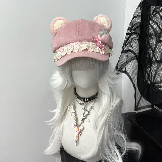 Pink newsboy cap with plush bear ears and white lace brim, decorated with a checkered cupcake patch, styled on a white wig with a gothic cross necklace.
