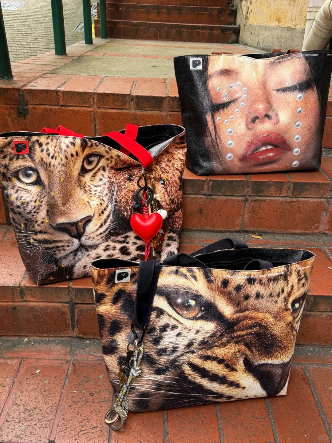 Three handbags with leopard and face designs on a brick surface.