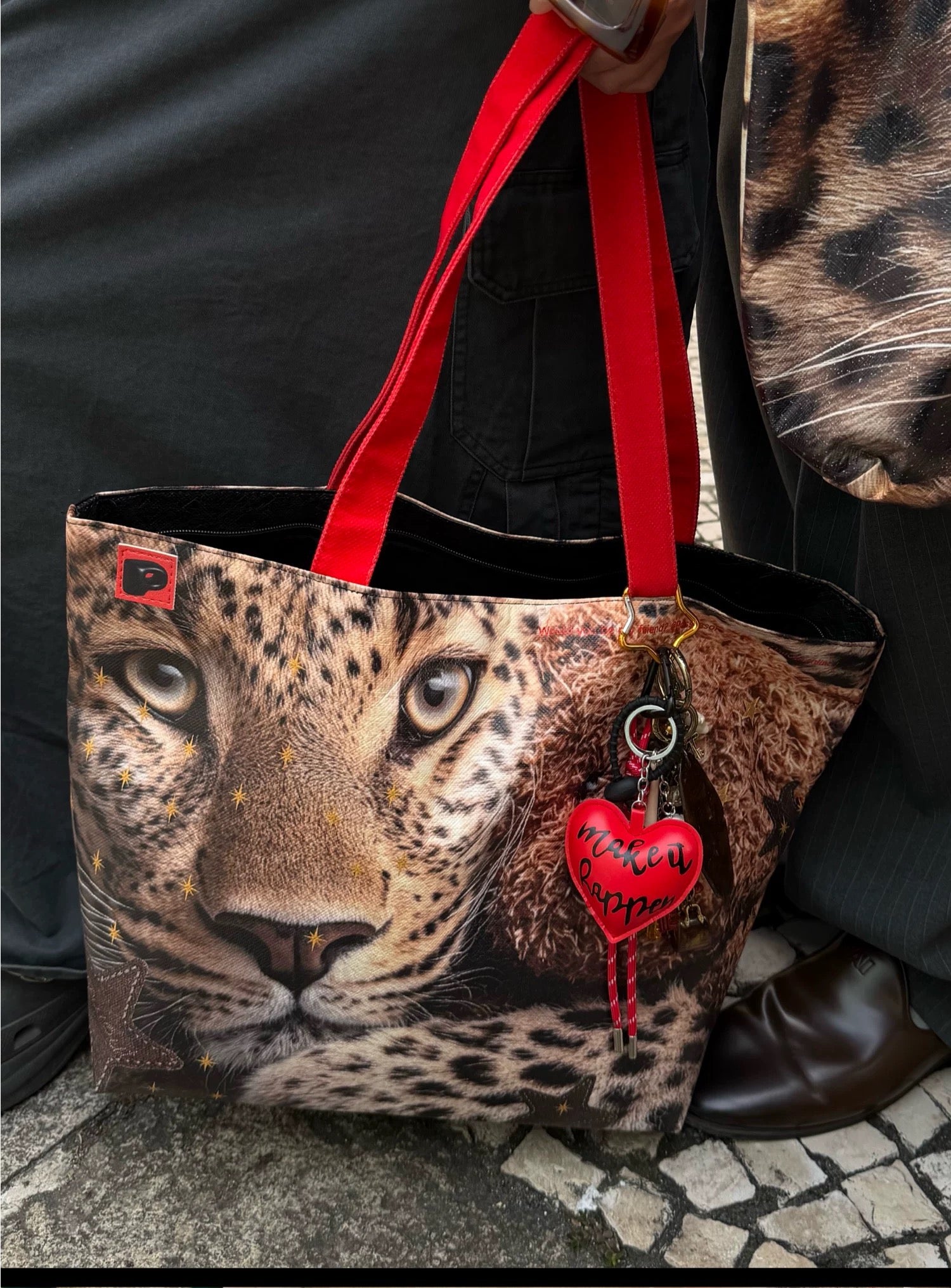Leopard print bag with red handle and heart-shaped tag held by a person wearing a leopard print coat.